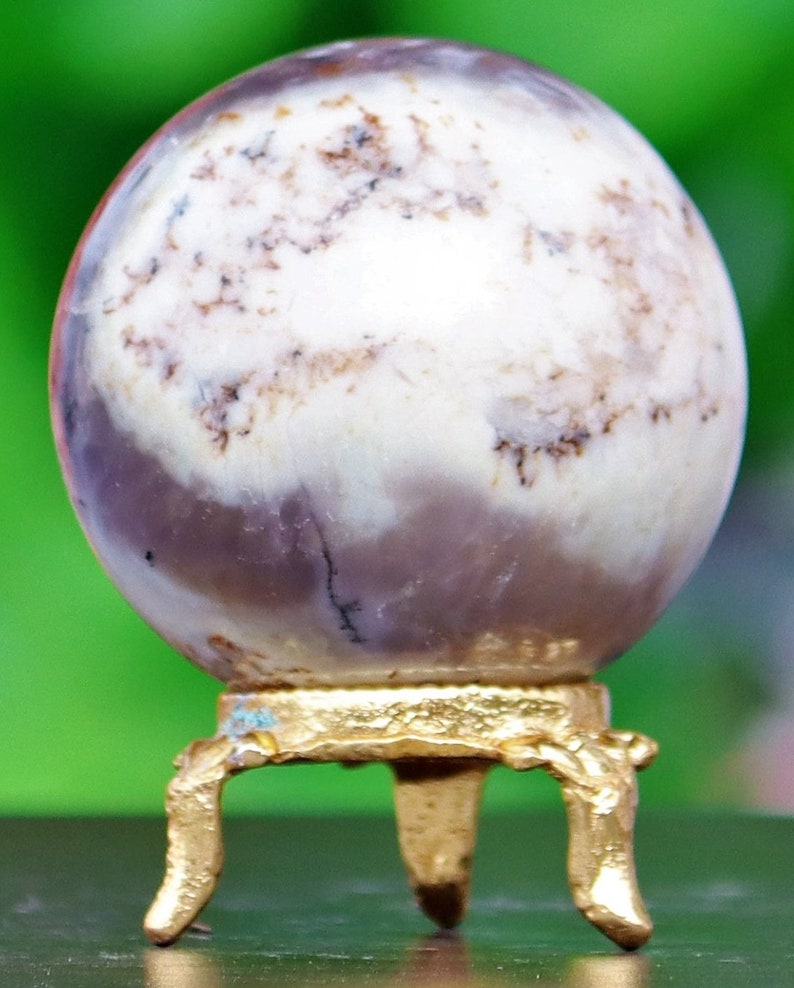 May include: A white and purple agate sphere on a gold metal stand with three legs. The sphere has a swirling pattern of white, purple, and brown.