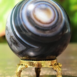 May include: A black and white agate sphere with swirling patterns sits on a gold metal stand with three legs.