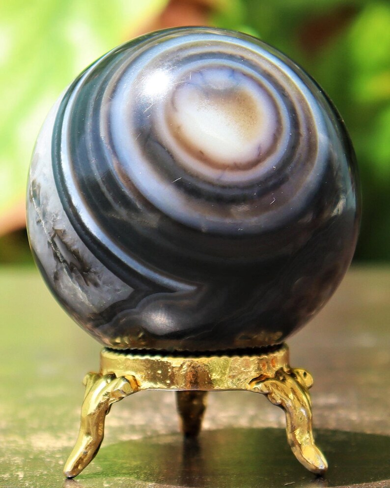 May include: A black and white agate sphere with swirling patterns sits on a gold metal stand with three legs.