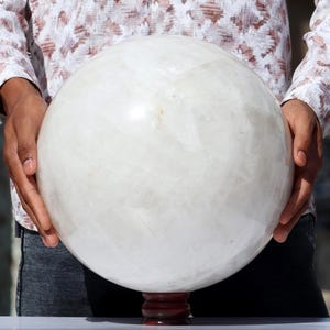 May include: A large, white, crystal ball on a wooden stand. The ball is smooth and polished, and it reflects light.