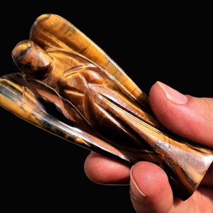 Peut inclure: Une figurine d'ange sculpt&eacute;e en pierre d'&oelig;il de tigre. L'ange a des ailes d&eacute;taill&eacute;es et une expression sereine. La pierre pr&eacute;sente des bandes de marron, d'or et de noir.