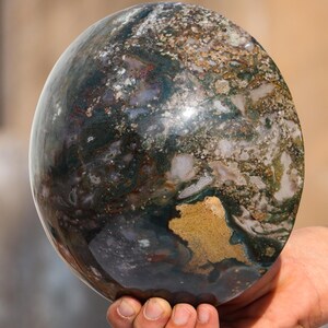 May include: A large, polished sphere of green, brown, and white moss agate. The sphere has a smooth, shiny surface and intricate patterns of colour.