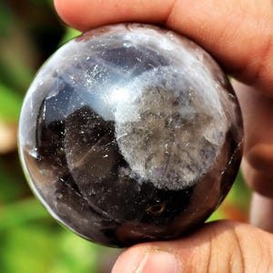 Può includere: Una sfera di cristallo liscia, nera e bianca con un centro bianco nuvoloso. La sfera è lucidata e ha una superficie riflettente.