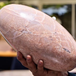 Puede incluir: Una piedra grande, lisa, de forma ovalada con un patrón de mármol rosa y blanco.