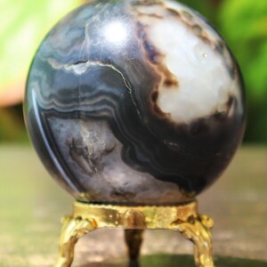May include: A polished black and white agate sphere on a gold metal stand. The sphere has a swirling pattern of black and white bands.