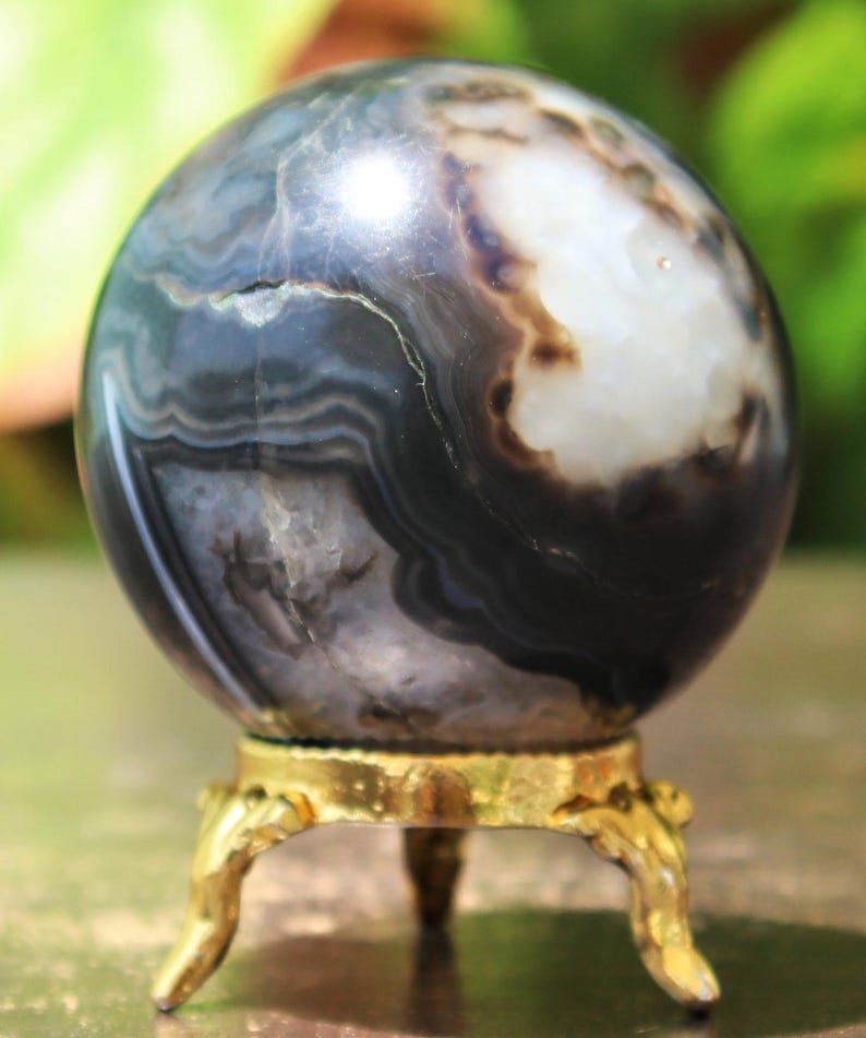 May include: A polished black and white agate sphere on a gold metal stand. The sphere has a swirling pattern of black and white bands.