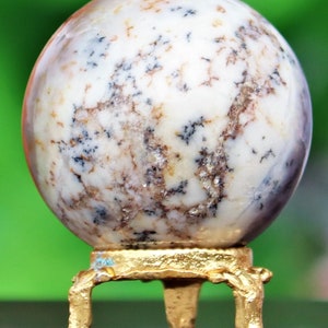May include: A white agate sphere with brown and black markings, displayed on a gold metal stand with three legs.