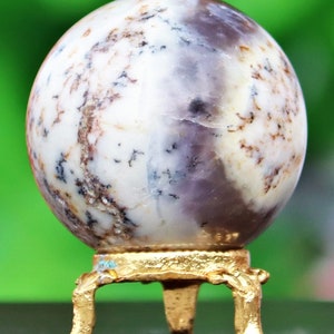 May include: A white and purple agate sphere on a gold metal stand with three legs. The sphere has a swirling pattern of white, purple, and brown.