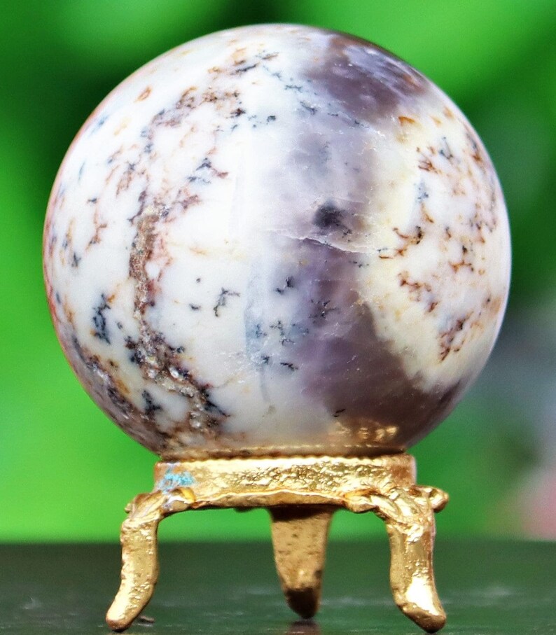May include: A white and purple agate sphere on a gold metal stand with three legs. The sphere has a swirling pattern of white, purple, and brown.