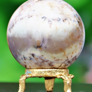 May include: A white agate sphere with brown and black markings sits on a gold metal stand with three legs.