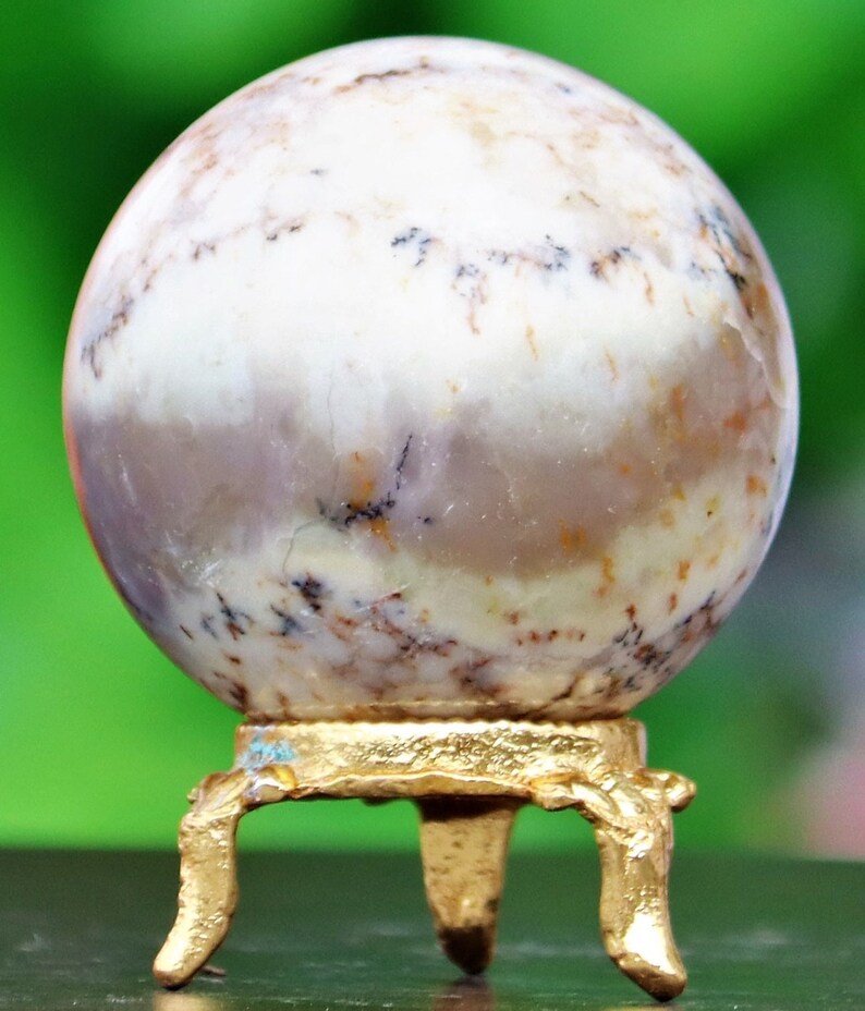 May include: A white agate sphere with brown and black markings sits on a gold metal stand with three legs.