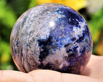 May include: A polished sphere with a marbled appearance, featuring a blend of deep blue, gray, and white hues. The surface has a glossy finish with flecks of gold. The sphere is a decorative item, possibly a paperweight or a collectible.