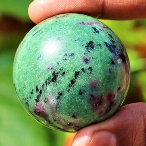 Könnte beinhalten: Grüne, schwarze und rosafarbene Edelsteinkugel. Die Kugel ist glatt und poliert.