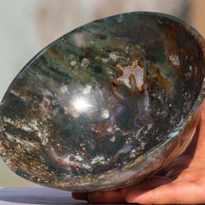 May include: A green, brown and white agate bowl with a swirling pattern. The bowl is made of natural stone and has a smooth, polished finish.