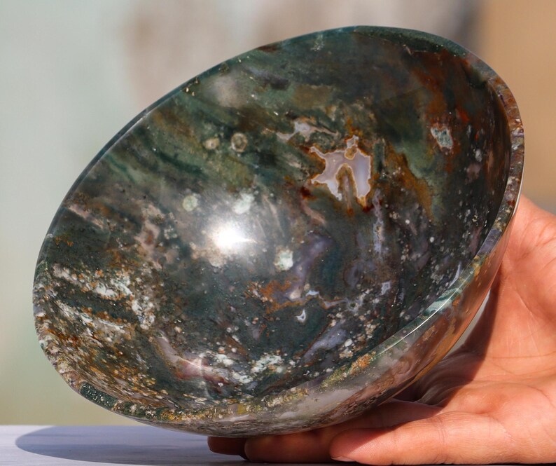 May include: A green, brown and white agate bowl with a swirling pattern. The bowl is made of natural stone and has a smooth, polished finish.