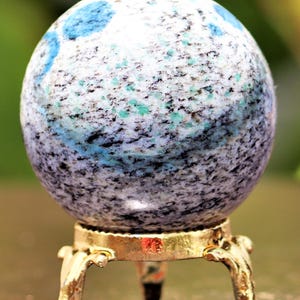 May include: A blue and white speckled sphere on a gold metal stand with three legs. The sphere is made of a natural stone.