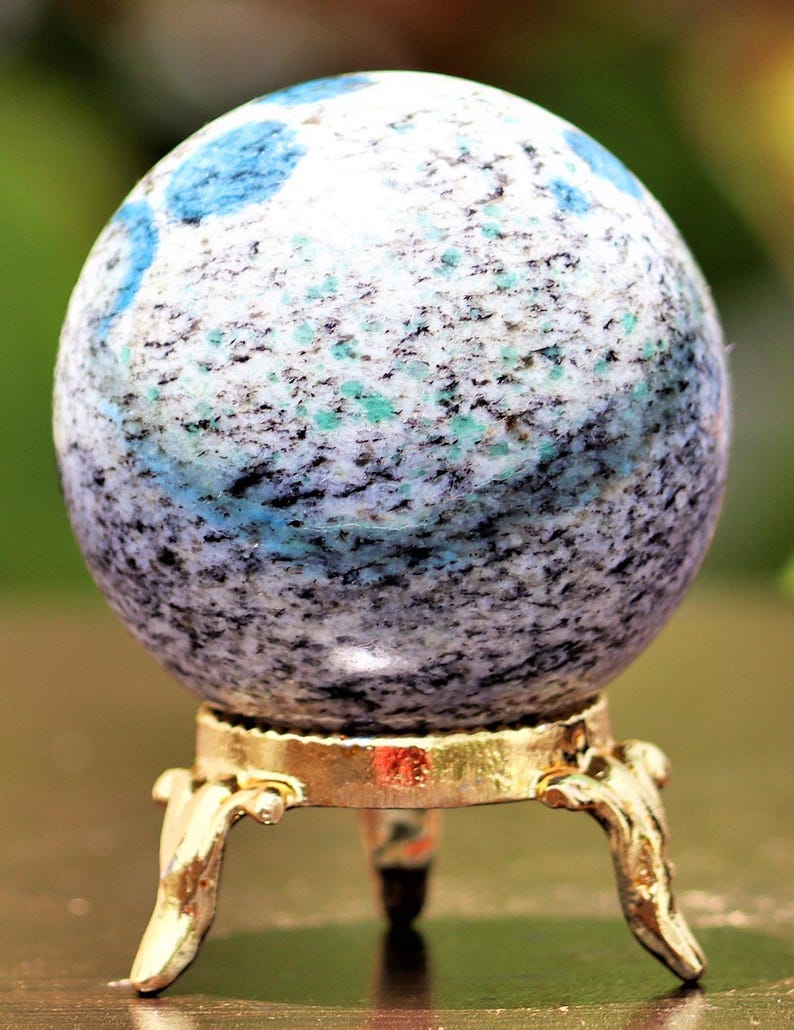 May include: A blue and white speckled sphere on a gold metal stand with three legs. The sphere is made of a natural stone.