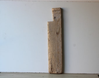 Può includere: Una tavola di legno di colore marrone chiaro e usurata con una forma unica, che presenta un taglio nella parte superiore. La tavola è appoggiata a un muro bianco.