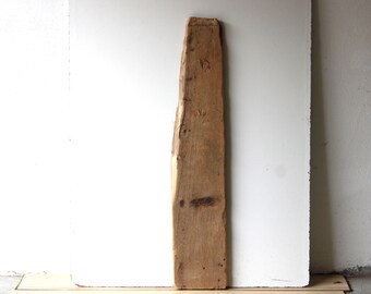 Può includere: Un pezzo lungo e stretto di legno invecchiato con una superficie ruvida e irregolare. Il legno è di colore marrone chiaro con nodi e motivi di venatura marrone scuro.