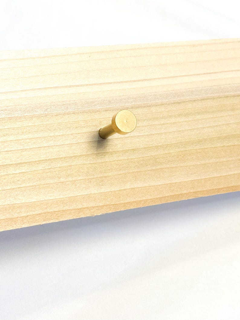 May include: A gold-toned metal hook mounted on a light wood surface.