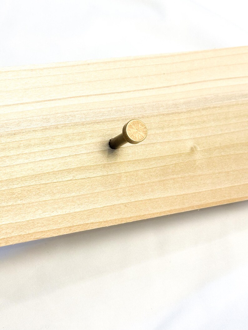 May include: A single brass hook mounted on a light wood surface.
