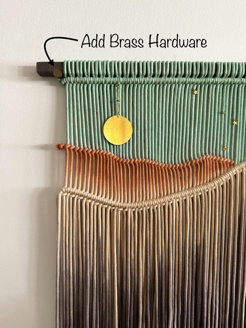 May include: A macrame wall hanging with a green, orange, and brown color gradient. The hanging features a brass circle and gold stars. The text "Add Brass Hardware" is written on the top of the image.