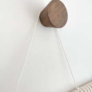 May include: A wooden wall hook with a rounded top, attached to a white wall with a white rope hanging from it.