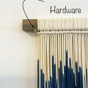 May include: A white and blue macrame wall hanging with a wooden dowel and brass hardware. The hanging is made with cotton cord and has a ombre effect with the blue color fading into the white.