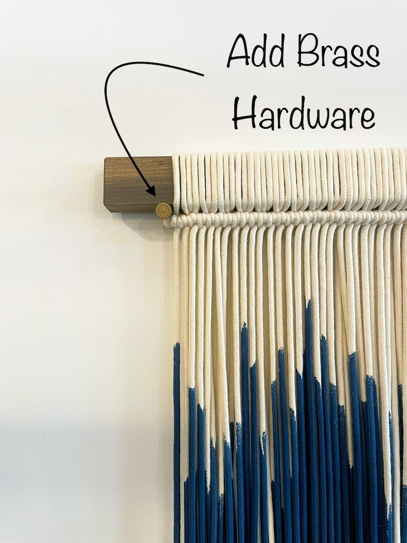 May include: A white and blue macrame wall hanging with a wooden dowel and brass hardware. The hanging is made with cotton cord and has a ombre effect with the blue color fading into the white.