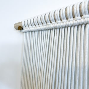 May include: White macrame wall hanging with a wooden dowel rod and brass finial.