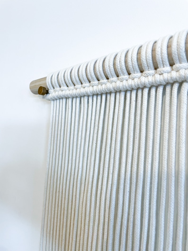 May include: White macrame wall hanging with a wooden dowel rod and brass finial.