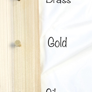May include: Three metal hooks in brass, gold, and silver finishes mounted on a wooden board.