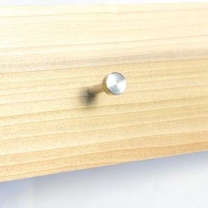 May include: A silver metal hook with a round head, mounted on a light brown wooden surface.