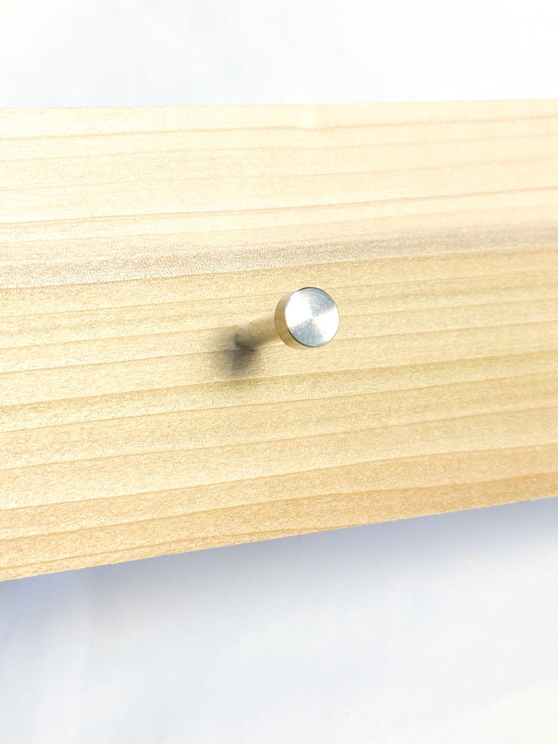 May include: A silver metal hook with a round head, mounted on a light brown wooden surface.