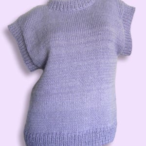 Könnte beinhalten: Ein fliederfarbener Pullover mit kurzen Ärmeln, geripptem Saum und Ausschnitt. Das Strickoberteil hat einen Rundhalsausschnitt und eine leicht ausgestellte Form. Das Kleidungsstück wird auf einer Schaufensterpuppe präsentiert.