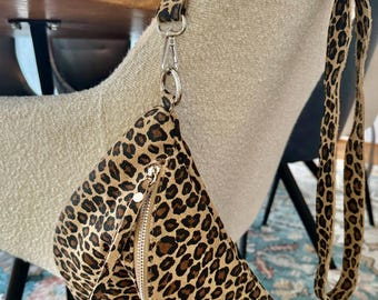 Puede incluir: Un bolso de cintura con estampado de leopardo con cierre de cremallera y correa ajustable. La bolsa presenta un patrón de manchas marrones y negras y un cierre de metal plateado. La correa está sujeta a la bolsa con un cierre de metal plateado.