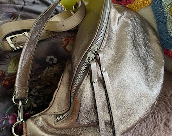 May include: A silver metallic fanny pack with a zipper closure and a long strap. The bag is made of leather and has a shiny finish.