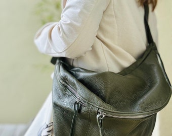 Könnte beinhalten: Eine dunkelgrüne Leder-Umhängetasche mit Reißverschluss und langen Quasten. Die Tasche wird über der Schulter einer Person getragen, die ein weißes Hemd trägt.
