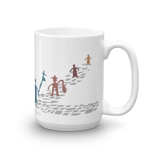 May include: A white ceramic mug featuring a graphic illustration of four stylized figures walking along a gray cobblestone path. The figures are rendered in blue, brown, and tan colors, with one figure carrying a bag and another holding a tall staff.