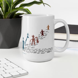 May include: A white ceramic mug featuring a graphic of four stylized figures walking along a gray cobblestone path. The figures are colored in blue, brown, dark red, and orange, with some carrying bags. The design includes small text near the base.