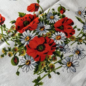 May include: White linen fabric with a floral pattern featuring red poppies, white daisies, and yellow accents. Green leaves and stems complete the design. The flowers are clustered together, creating a vibrant and colorful display.