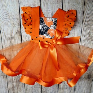 May include: Orange tulle dress with black polka dots and a pumpkin print bodice. The dress has a satin ribbon bow and a satin trim around the bottom.
