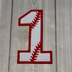 May include: White felt number one with red baseball stitching. The number is a baseball-themed applique.