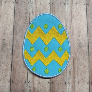 May include: A blue and yellow embroidered Easter egg patch with a zig-zag pattern and green dots.