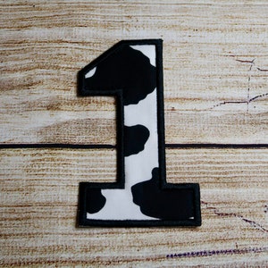 May include: A black and white cow print fabric patch in the shape of the number one.