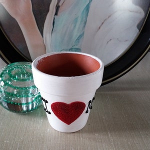 May include: White ceramic flower pot with a red heart and the words "I Love NY" in black lettering.