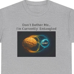 Puede incluir: Camiseta gris con el texto "Don't Bother Me... I'm Currently Entangled". La camiseta presenta un gráfico de un cerebro, un símbolo "Qubit" y líneas onduladas amarillas y azules.