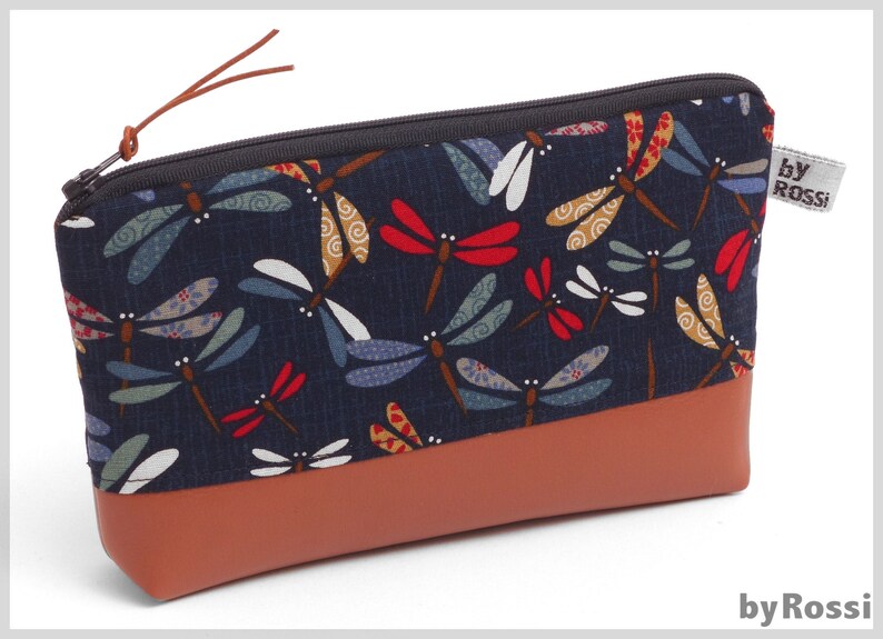 May include: A blue and brown zippered pouch with a dragonfly pattern and the text "by Rossi" on the side.