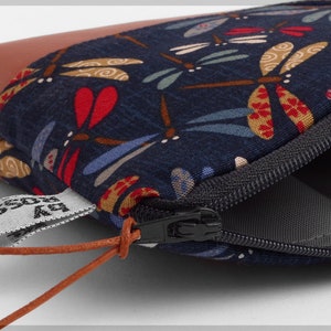 May include: A small zippered pouch with a brown leather flap and a blue fabric lining featuring a dragonfly pattern. The pouch has a brown leather cord with a tag that reads "by Rossi".