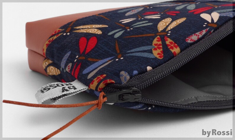 May include: A small zippered pouch with a brown leather flap and a blue fabric lining featuring a dragonfly pattern. The pouch has a brown leather cord with a tag that reads "by Rossi".